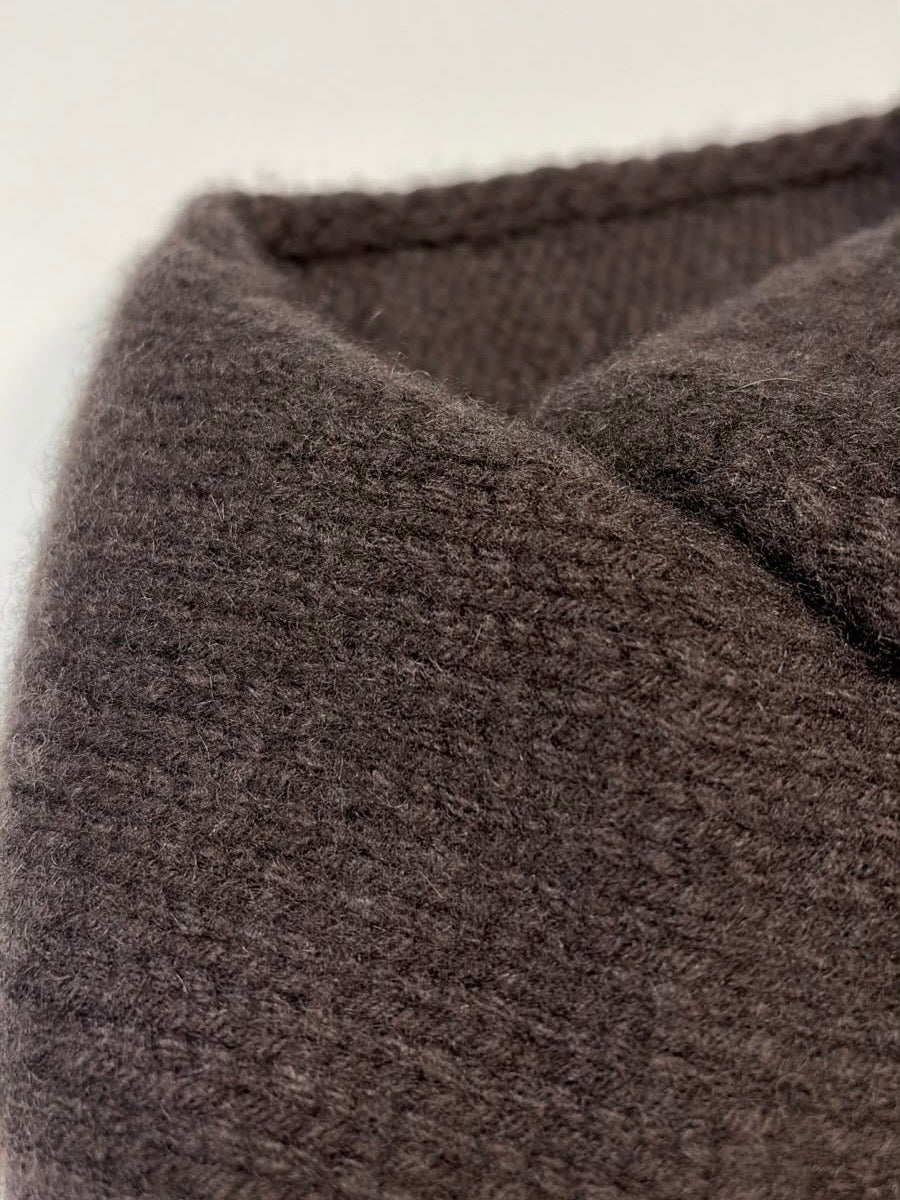 Close-up of a dark brown textured knit fabric, showing the detailed weave and collar stitching.