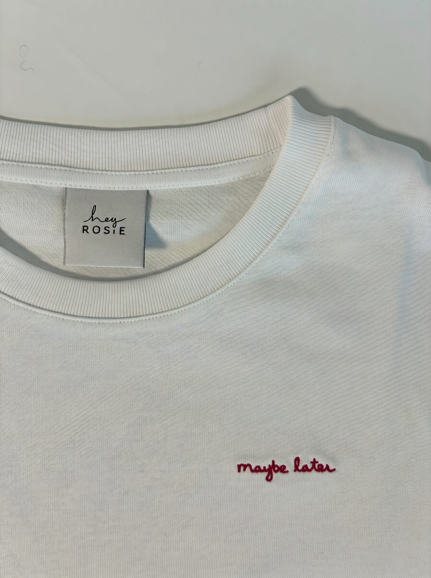 White sweatshirt with 'maybe later' embroidery and 'hey rosie' label on a white background